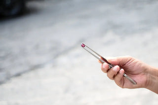 A hand holding a gemstone with tweezers, illustrating care for gemstone jewelry in Hawaii.