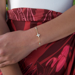 Close-up of a wrist wearing a gold bracelet with a white flower charm, against a red patterned fabric background.