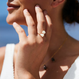 Close-up of a woman's hand wearing a unique white pikake flower ring with mother of pearl flowers.