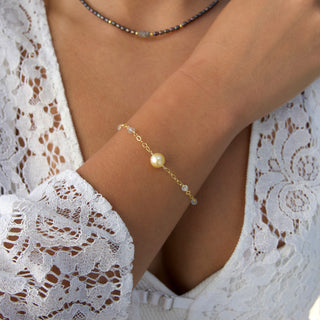 Close-up of a wrist wearing a delicate bracelet with a pearl on a lace garment.