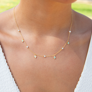 Gold necklace with small green gemstones worn by a person outdoors