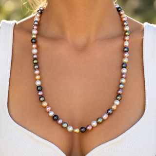 A multicolor freshwater pearl necklace worn by a model in a white ribbed tank top, photographed in a bright outdoor setting.