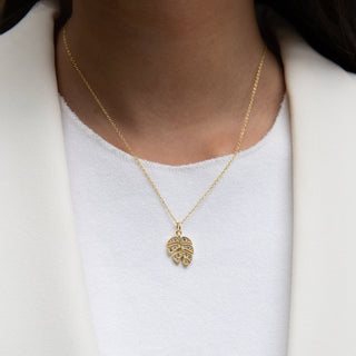 Gold necklace with a leaf pendant worn by a person on a white background