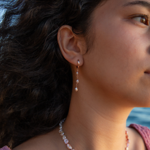 Load image into Gallery viewer, Model wearing Triple Pink Pearl Keshi Huggies earrings against a sunset background.