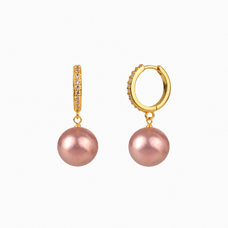 A pair of gold huggie hoop earrings with a pavé band and a dangling pink freshwater pearl, shown on a plain white background.
