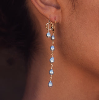 Pearl earring worn on an ear with a dark background