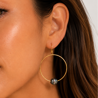 A close-up of a woman wearing a large gold hoop earring with a small dark gray bead at the bottom, shown against her ear and hair.