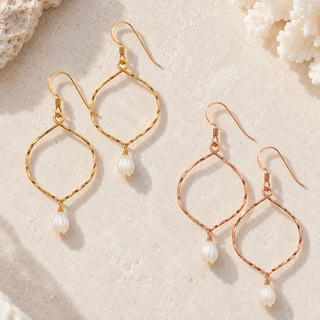 Three pairs of dangle earrings displayed on a light beige textured surface with coral props. The earrings feature twisted wire loops in gold and rose gold, each suspending a small white pearl drop.