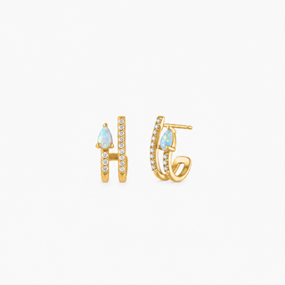 A pair of gold huggie hoop earrings with teardrop-shaped light blue opal gemstones and small pavé-set clear stones, shown against a plain white background.