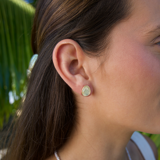 Close-up of a person wearing a moonstone stud earring with a blurred natural background