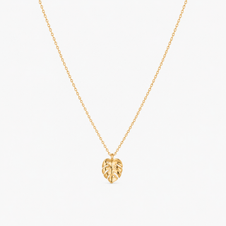 A delicate gold chain necklace featuring a small leaf-shaped pendant, displayed against a clean, light off-white background.