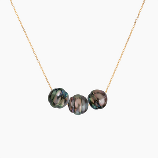 A delicate gold chain necklace featuring three round, peacock pearls in shades of green, gray, and purple, displayed against a solid off-white background.