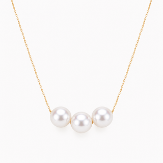 A delicate gold chain necklace featuring three lustrous white freshwater pearls aligned horizontally at the center, set against a clean, light off-white background.