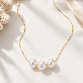 A delicate gold chain necklace featuring three lustrous white freshwater pearls arranged in a row, displayed on a textured white surface with soft shadows.
