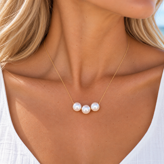 A close-up of a woman wearing a delicate gold chain necklace with three small, lustrous white pearls centered on the chest.