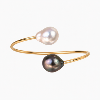 A gold-plated open cuff bracelet featuring two teardrop-shaped freshwater pearls, one lustrous white and one dark iridescent gray-black, set against a plain white background.